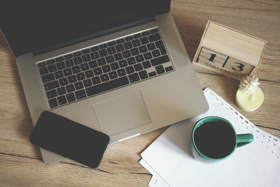 Modern office desk setup with laptop, smartphone, coffee, and calendar for productive work environment.